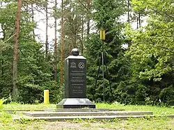 A stone pillar with the inscription about the site. Trees  behind.
