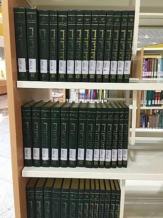 صورة لكتب ذات لون متجانس أخضر غامق مصفوفة بجانب بعضها البعض فوق ثلاثة رفوف