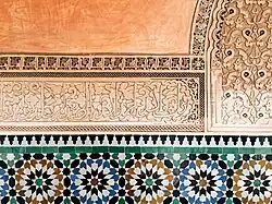 سورة الإخلاص منقوشة بالخط الثلث المغربي فوق الزليج وتحت التدلكت على جدار المدرسة