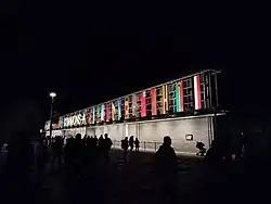 Visitors in front of a grey building with flags of various Asia–Pacific, African, and Caribbean nations