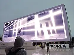 White building with a large panoramic screen and a Korea sign in front