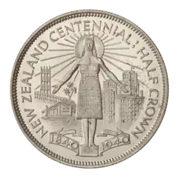 A coin featuring a Māori woman in a skirt standing between traditional and modern architecture. A sun and rays are behind her head. Below her is a ribbon reading "1840 – 1940". Around her is the encircling text "NEW ZEALAND CENTENNIAL HALF CROWN"