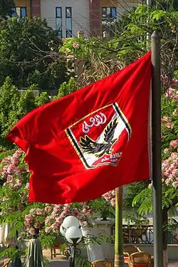 A flag with the crest of Egyptian association football club Al Ahly، on a red background، can be seen.