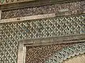 نقش عربي يمتد على طول الجزء العلوي من البوابة، مع مزيد من زخرفة الدرج والكتف والزليج أدناه