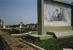 A park. On the right, a large structure with a black-and-white drawing of a man and boy crouching, the man waving, the boy holding onto the man's shirt.
