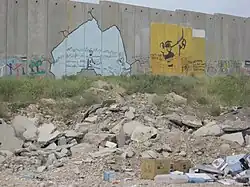 بانكسي إلى جانب لوحة جدارية له للزعيم الهندي غاندي - منطقة حاجز قلنديا