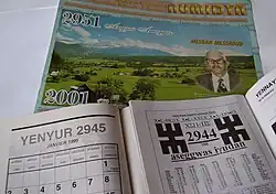 Three calendars are overlaid, with the most prominent displaying a page labeled "Yenyur 2945". Most of the visible text is written in the Berber Latin alphabet.