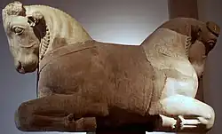 تُظهر الصورة العلوية عنصرين يمثلان عناصر معمارية ، تُظهر الصورة العلوية عمودًا كبيرًا مع بروتومات ثور تبرز من جانبيها. تُظهر الصورة السفلية عناصر عمود على شكل طارة موضوعة في حقل أخضر.