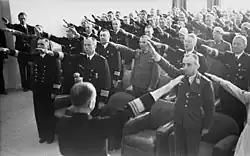 Photograph of dozens of Wehrmacht officers standing in a room and performing the Nazi salute