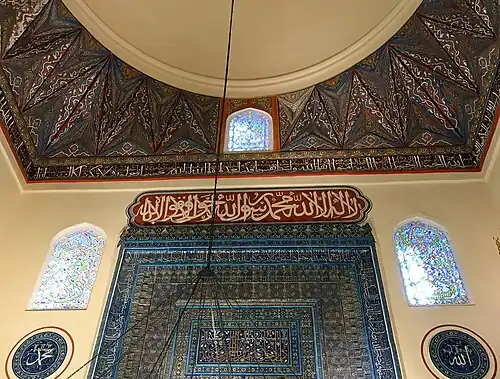 أعلى المحراب ويظهر جزء من القبة فوقه عليها زخارف على قاعدة القبّة وآيات قرآنية. النافذتان العلويتان، والنافذة في قاعدة القبّة فوق المحراب يرسلان الإضاءة الطبيعية إلى وسط الجامع.