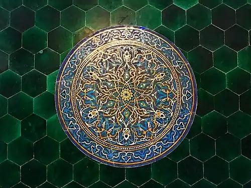 دائرة كبيرة من الزخرفة عربية (الأرابيسك) من الأزهار والنباتات، باللون الأزرق والأبيض والأسود والذهبي والأصفر، موجودة على إحدى جانبي الممر (الدهليز) المؤدي من باب الجامع إلى الردهة (الصالة الوُسطى).