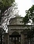باب المقبرة الحديدي وخلفه البناء الذي يعلو القبر.