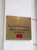 لافتة خارج مبنى السفارة باللغة العربية ولغة إنجليزية مع علم المغرب