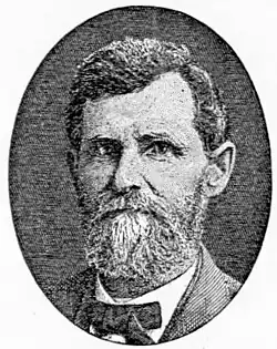 A middle-aged man with a graying beard is wearing a bow tie and suit jacket