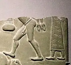 رجل في ثوب منقوش ومهدب خلف سجين عارٍ.