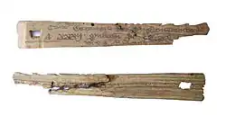Two small pieces of wood, slightly triangular in shape; these are two halves of the same piece of wood. The top piece shows writing in old English; the lower is rougher.