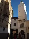 مسجد المزلجة، تعلوه لوحة زخرفية من الكوفي المربع فوق مدخله (يمين).