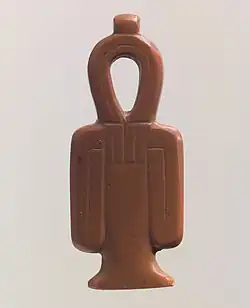 A red stone amulet shaped like a column with a looped top and two loops hanging at the sides