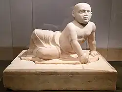 تمثال من الرخام لطفل من العائلة المالكة يبلغ من العمر حوالي سنتين، متمدد على جنبه الأيسر. والطفل حليق الرأس، وعيناه تحدقان إلى الأمام، الجزء الأسفل من جسمه ملفوف بقطعة من القماش تتدلى بين قدميه الهزيلتين. يدعم الطفل جذعه بيده اليسرى والتي يحمل بها شيئاً غير معروف، كما أنه يحمل طائراً صغيراً بيده اليمنى. التمثال موضوع على قاعدة ثقيلة منقوش على الجزء العلوي منها حروف بالكاد تكون مرئية بطريقة عمودية. يعوج التمثال لعام 400 ق. م.